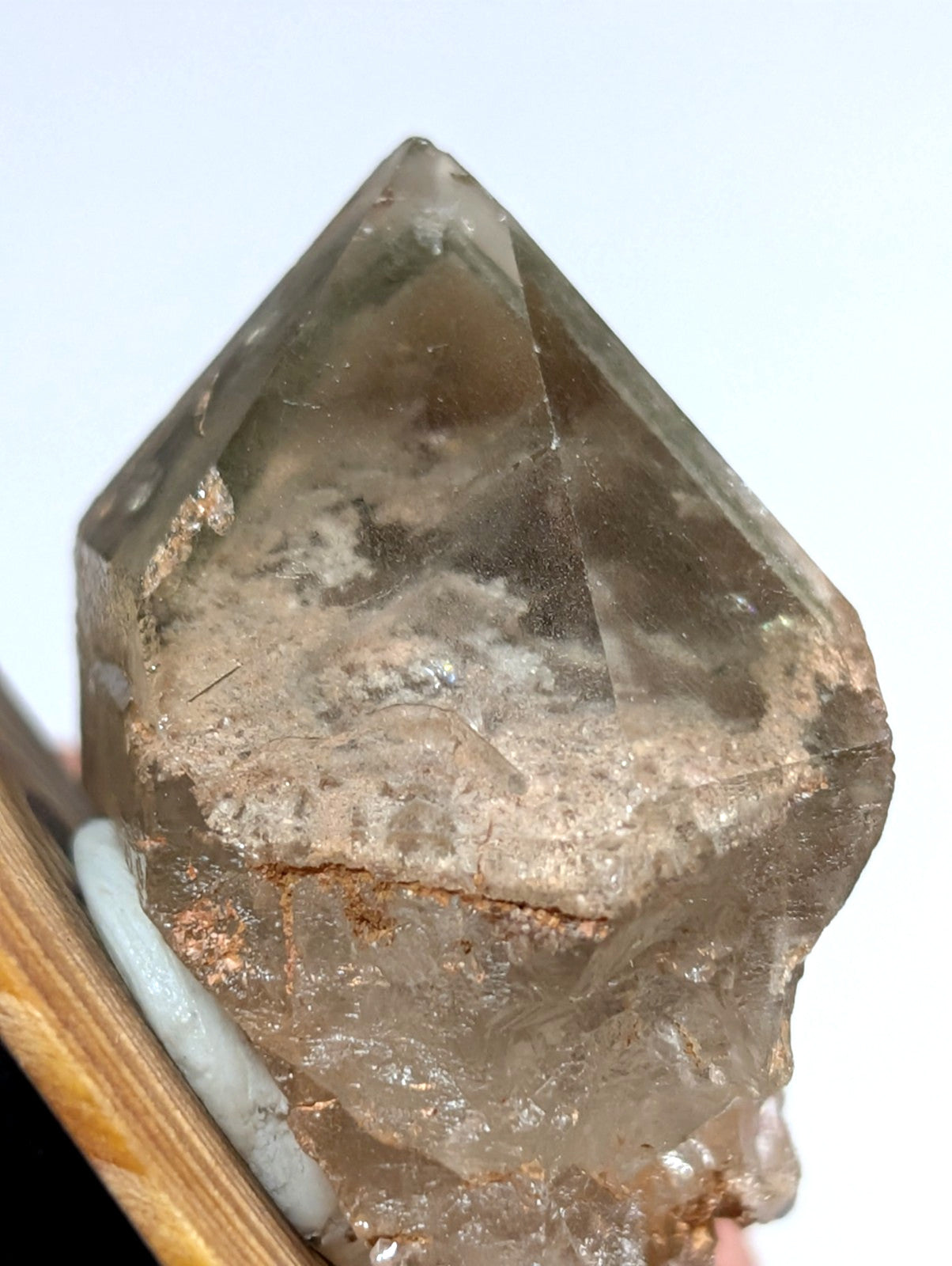 A translucent smoky quartz crystal with a pointed, faceted top and rougher base.