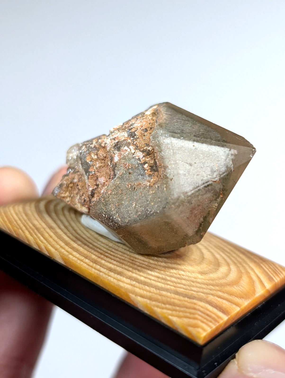 A translucent, faceted mineral specimen with a brownish-gray hue and rough, earthy matrix.