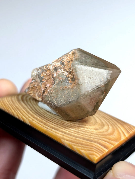 A translucent, faceted mineral specimen with a brownish-gray hue and rough, earthy matrix.