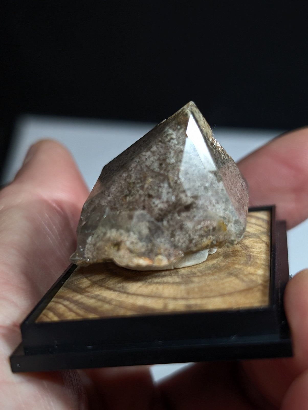 A translucent, faceted quartz crystal with a grayish hue and subtle golden inclusions rests on a wooden display base.