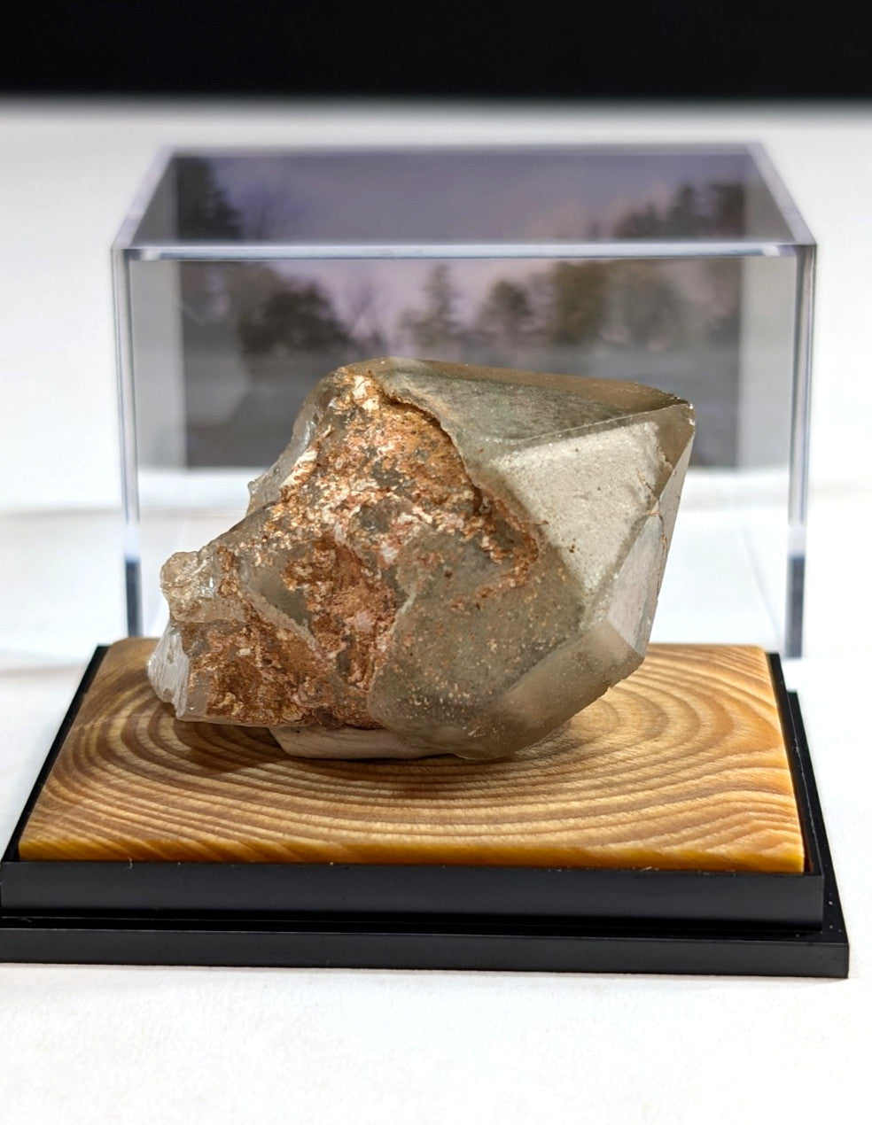 A translucent, faceted mineral specimen with golden-brown inclusions rests on a wooden display base.