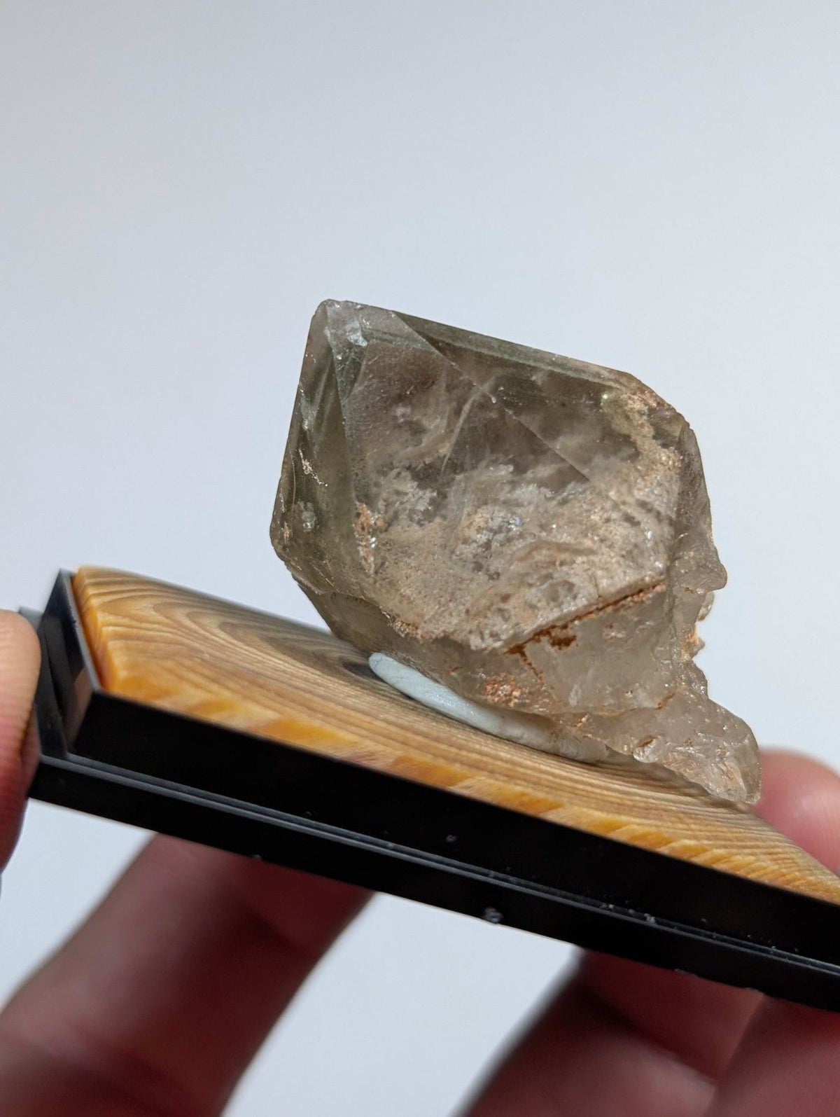 A translucent, smoky quartz crystal with a rough, faceted surface and visible internal inclusions rests on a wooden display stand.