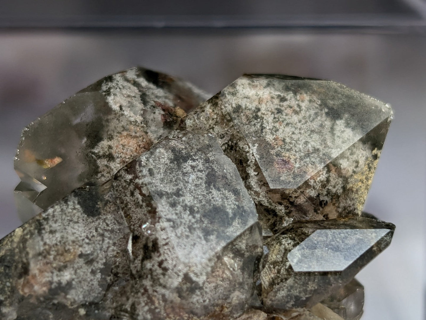 A cluster of translucent, grayish-green quartz crystals with speckled mineral inclusions and sharp geometric facets.