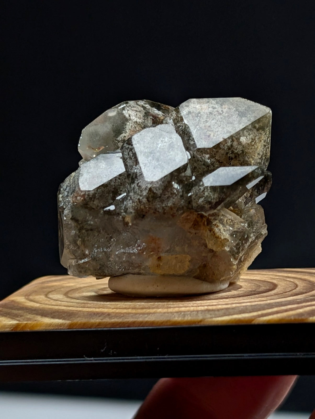 A translucent, multi-faceted quartz crystal cluster with a mix of clear and smoky gray tones, set on a wooden display base.