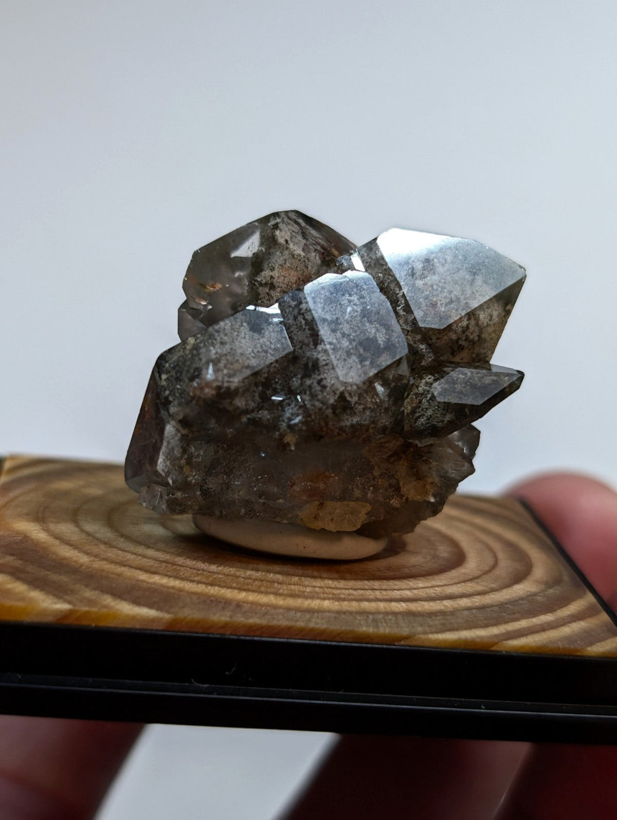 A cluster of dark, translucent quartz crystals with sharp geometric facets and a slightly rough, earthy base.