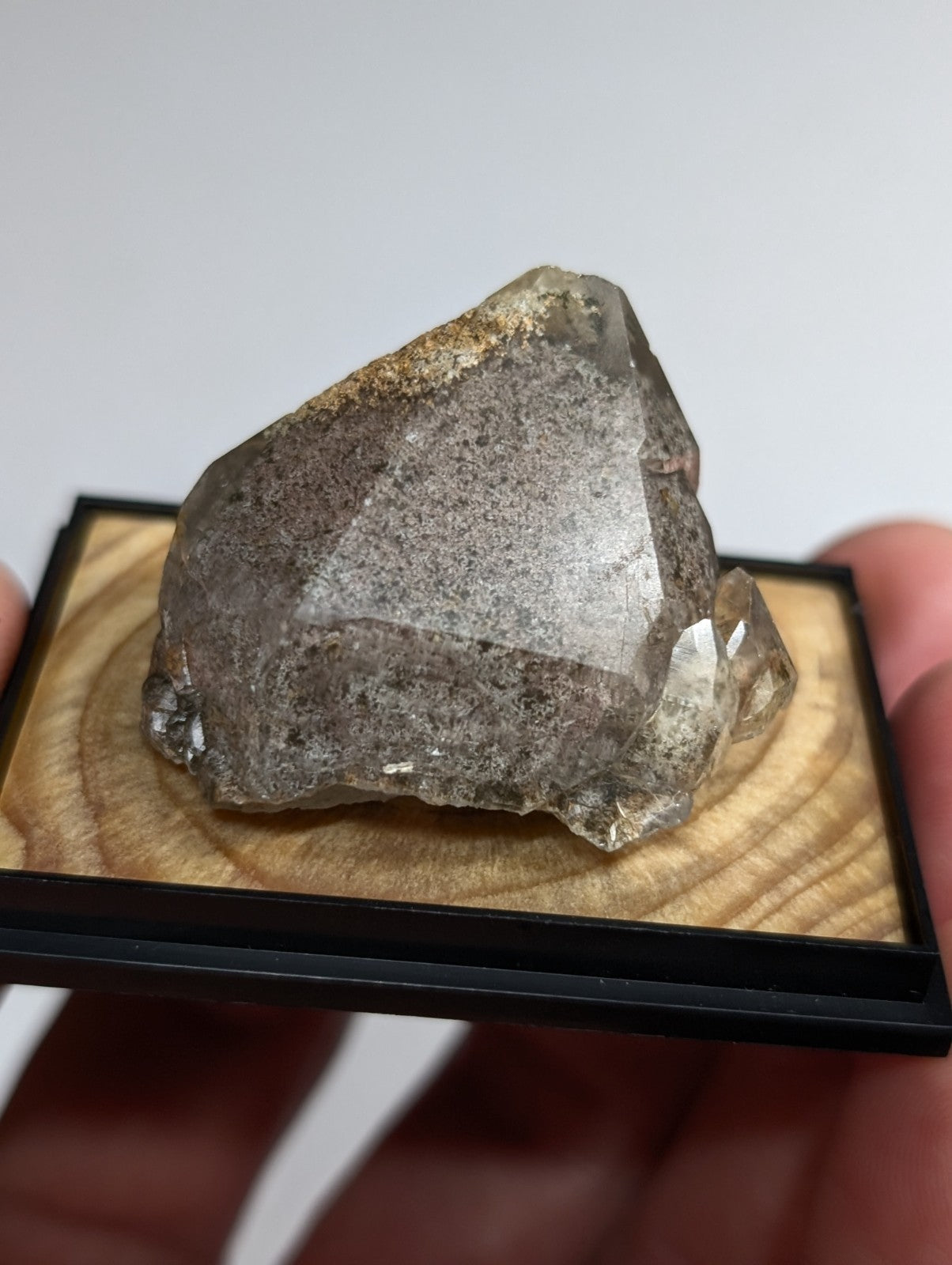 A translucent gray quartz crystal with a rough, faceted surface and subtle brownish inclusions rests on a wooden display base.
