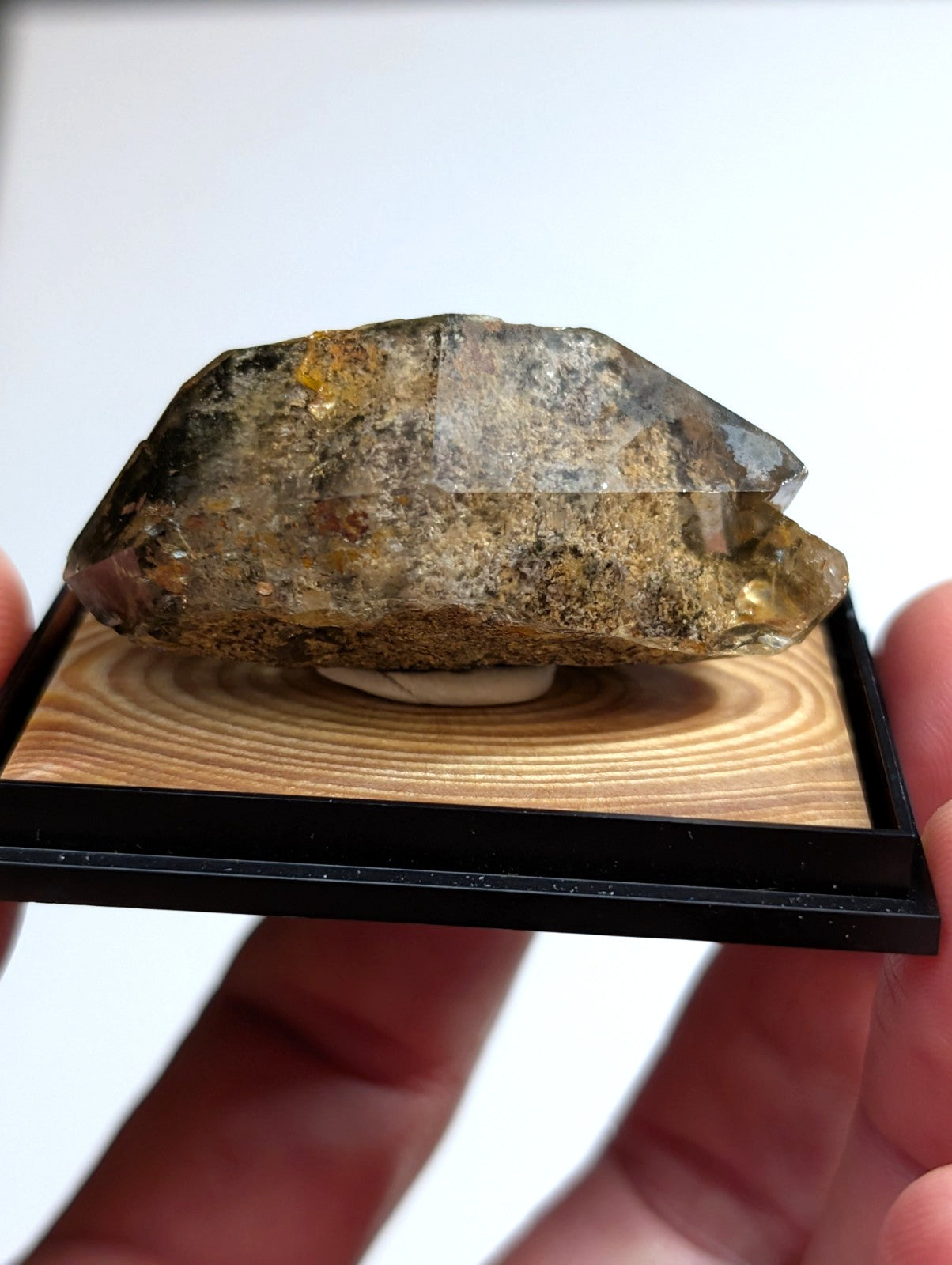 A translucent, earthy-toned quartz crystal with golden inclusions rests on a wooden display base.