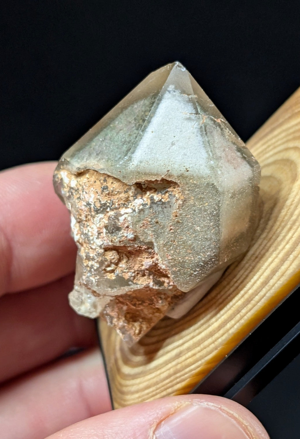 A translucent, faceted quartz crystal with a rough, earthy matrix of brown and gray mineral deposits.