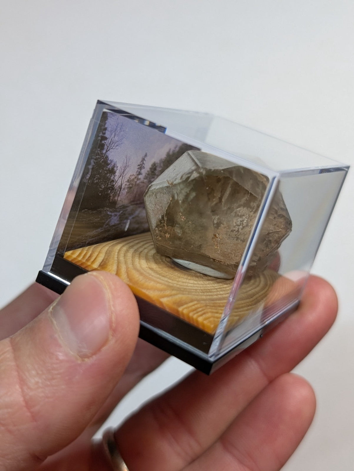 A translucent, faceted brown crystal displayed in a clear acrylic cube with a wooden base.