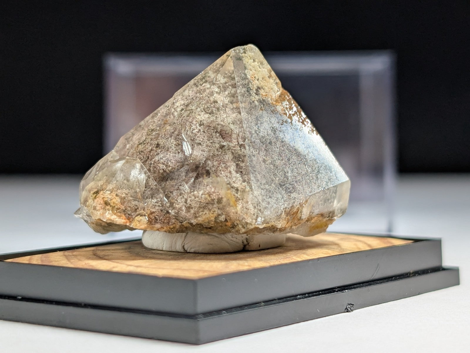 A translucent, faceted quartz crystal with earthy brown and gray veining rests on a wooden display base.