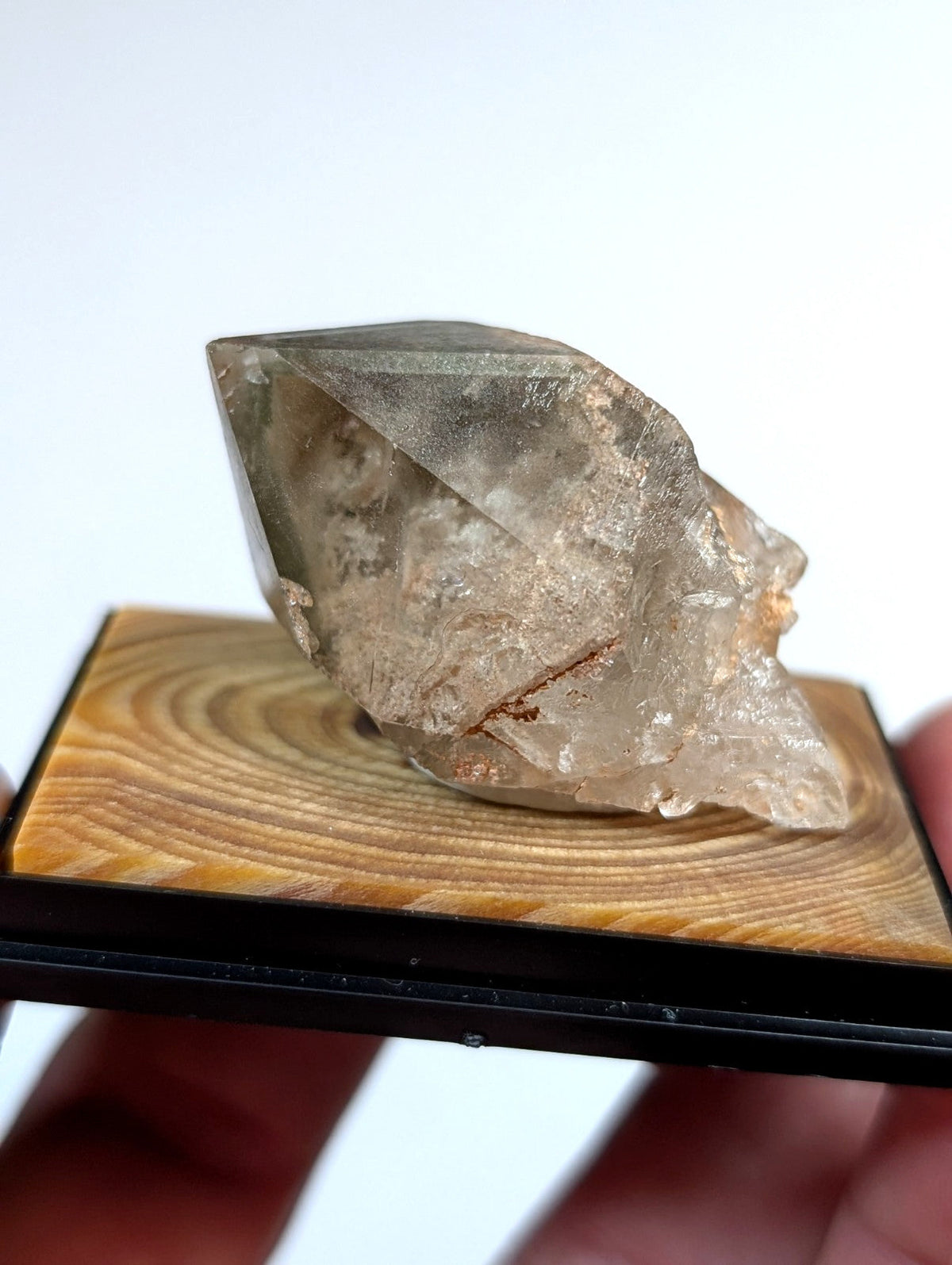 A translucent, faceted quartz crystal with subtle golden inclusions rests on a wooden display base.