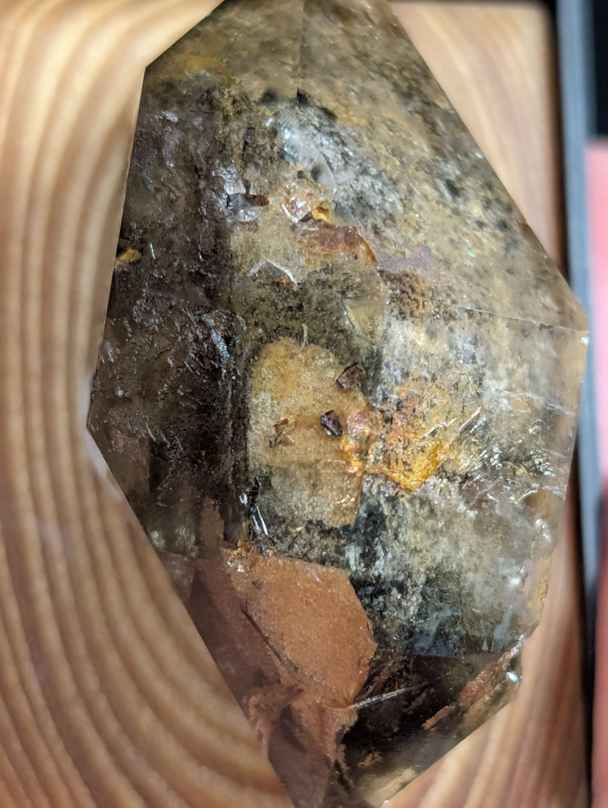 A faceted smoky quartz crystal with natural inclusions and earthy tones, showcasing a translucent amber core surrounded by darker mineral matrix.