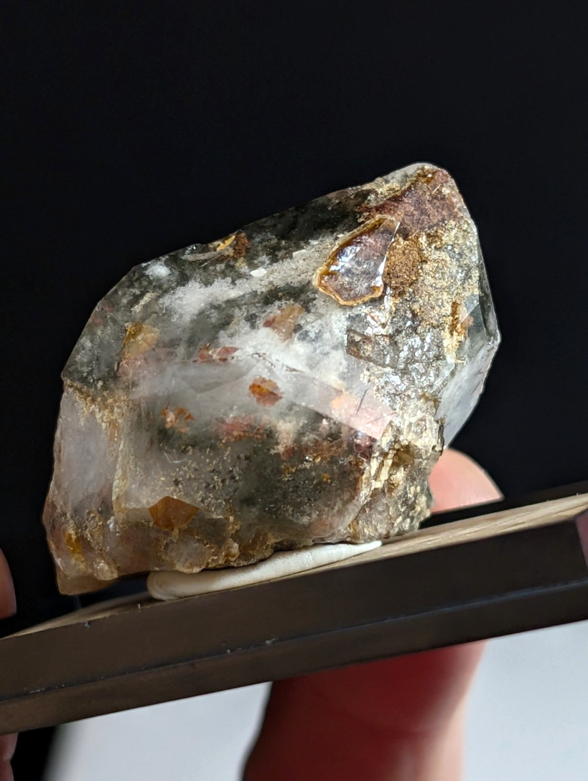 A translucent, rough-hewn crystal with embedded golden and reddish-brown mineral inclusions.