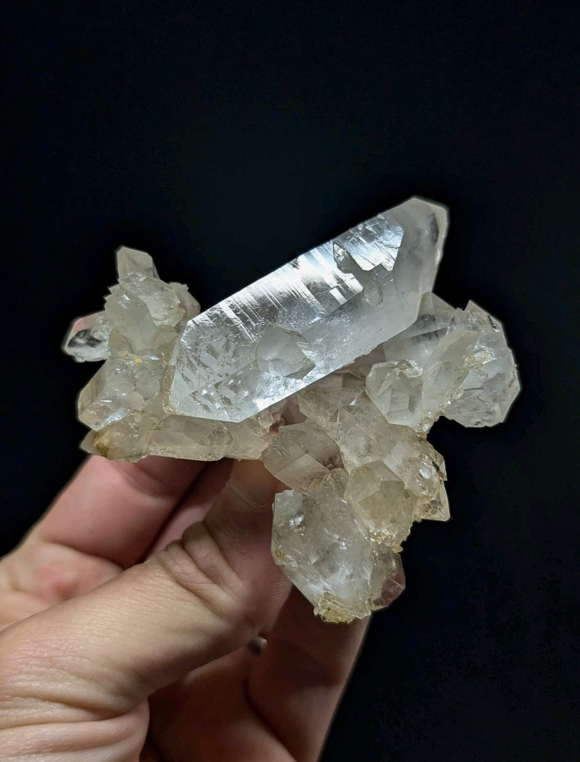 A translucent, clear quartz crystal cluster with a prominent central point and smaller surrounding crystals.