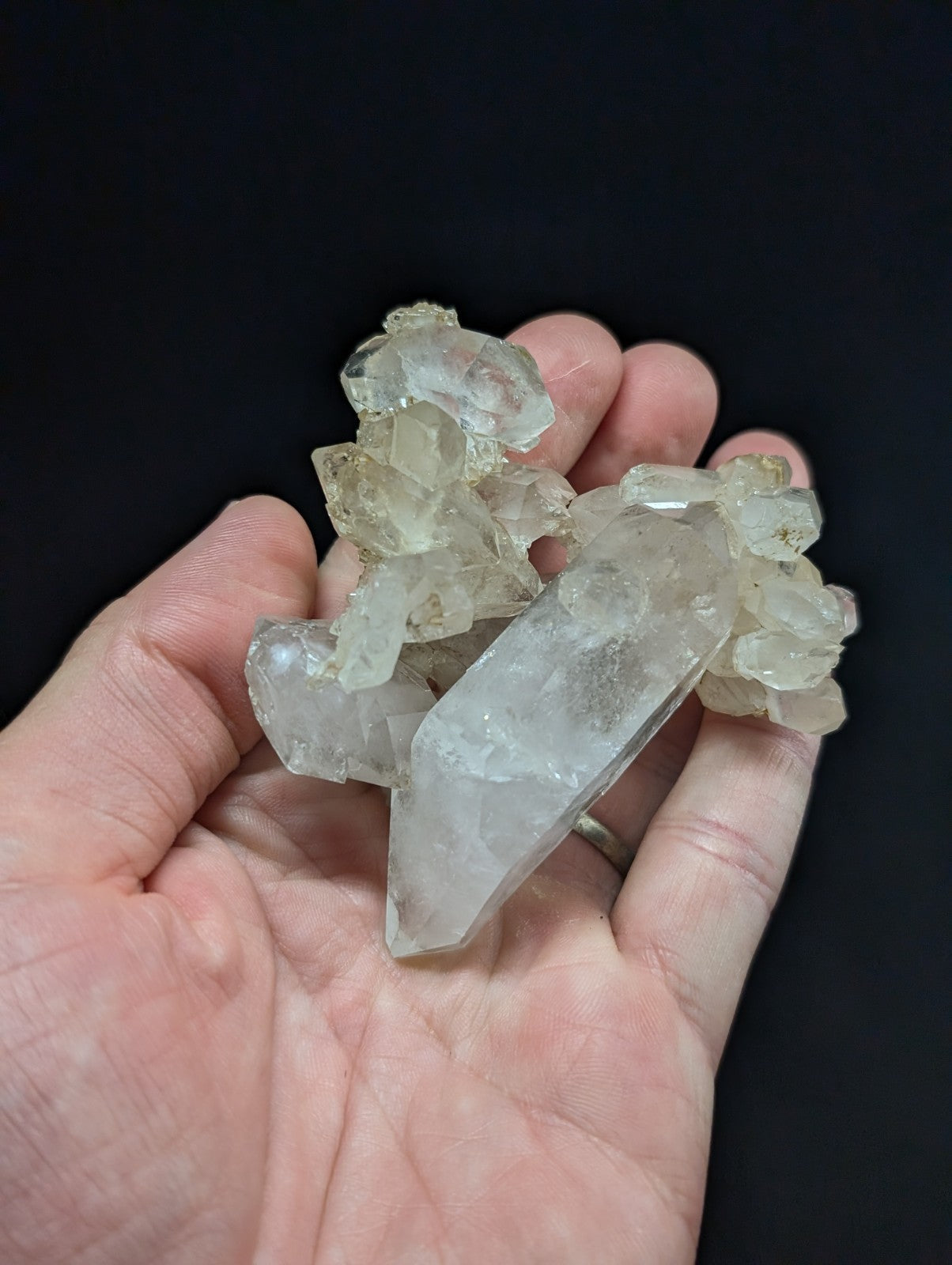 A cluster of translucent, clear quartz crystals with natural facets and slight yellowish tint held in a hand.