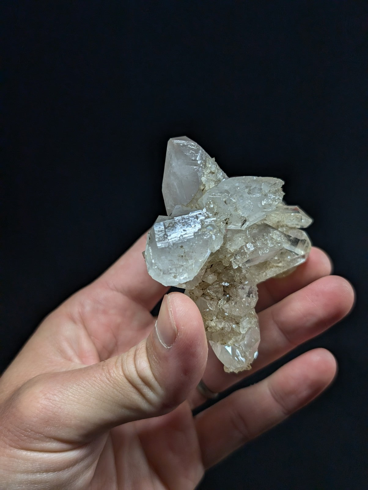 A translucent, clear quartz crystal cluster with sharp facets and a natural, earthy base.