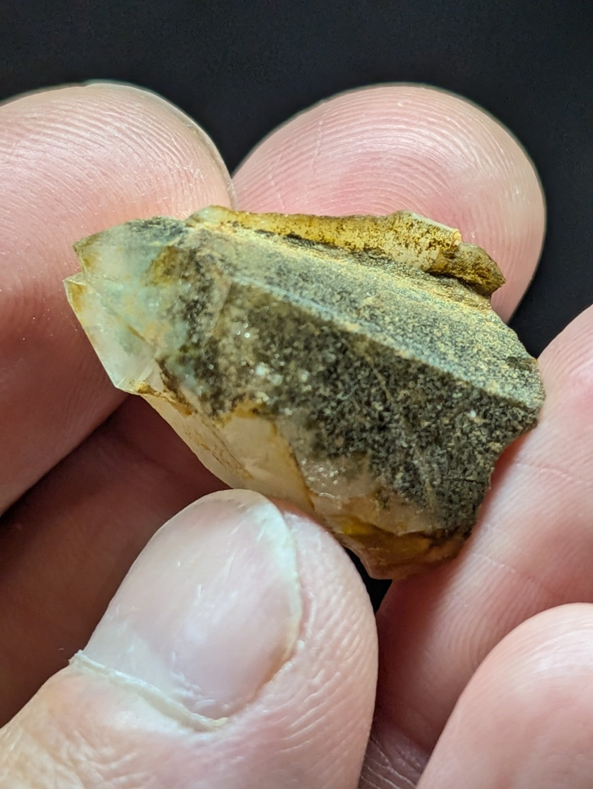 A translucent, pale yellow crystal with a rough, earthy greenish-brown coating and jagged edges.