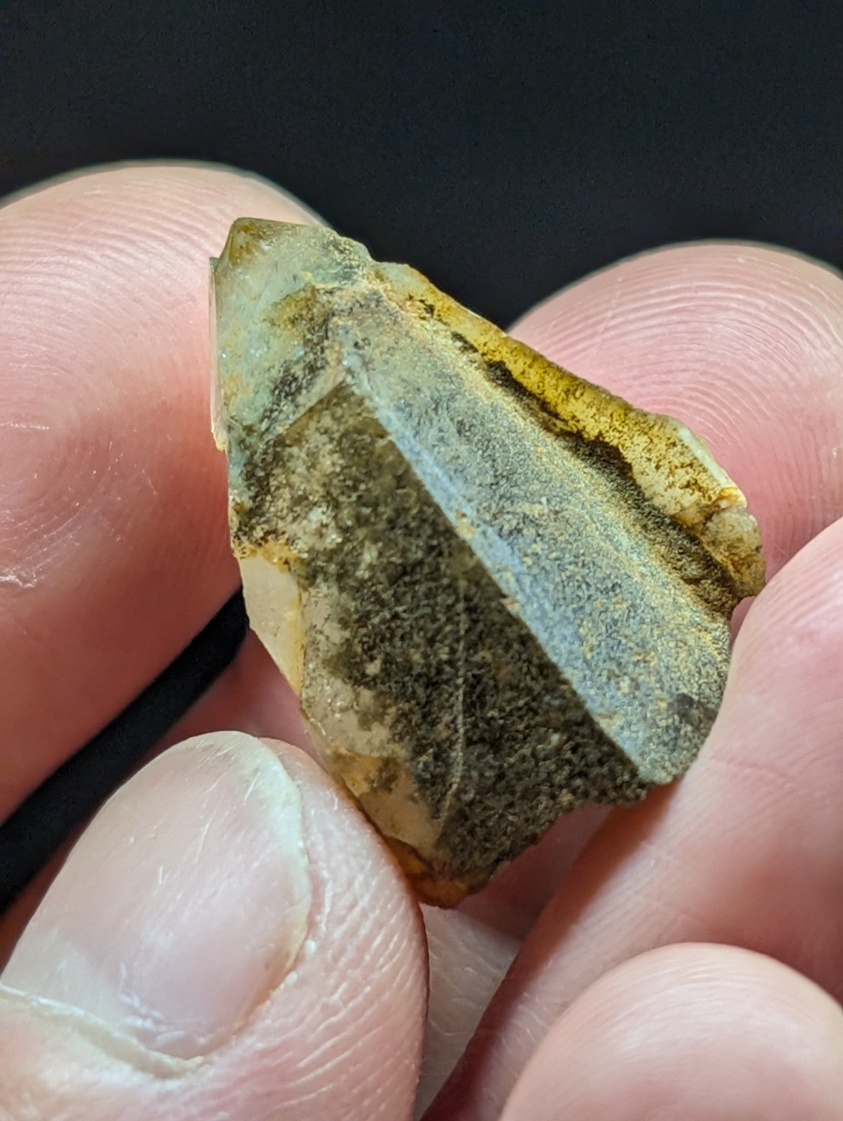 A translucent greenish-yellow crystal fragment with a rough, jagged surface and visible mineral inclusions.