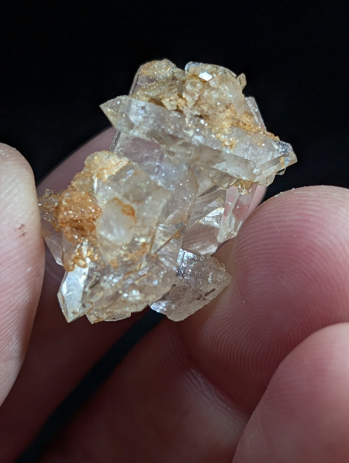 A cluster of translucent quartz crystals with golden mineral inclusions, held delicately between fingers.