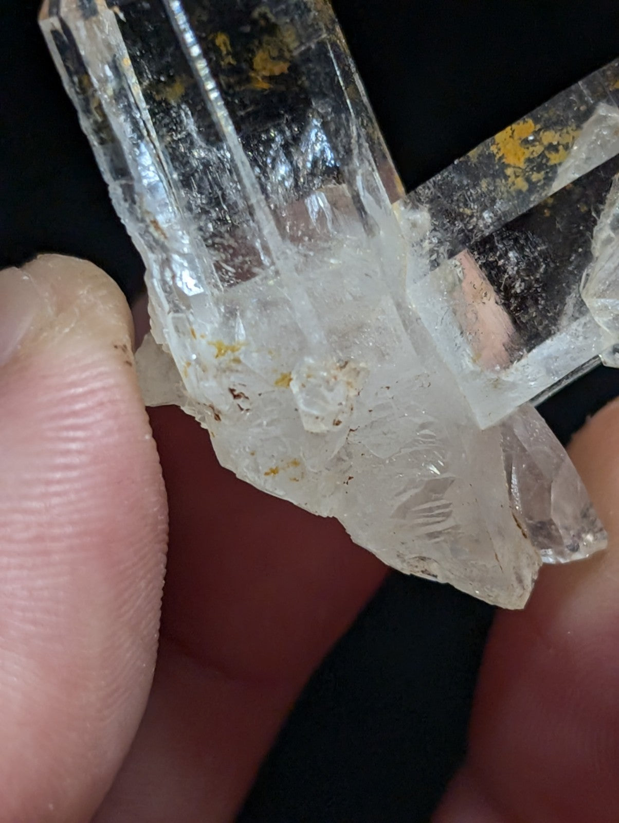 A clear quartz crystal cluster with natural facets and subtle yellow inclusions, held gently between fingers.