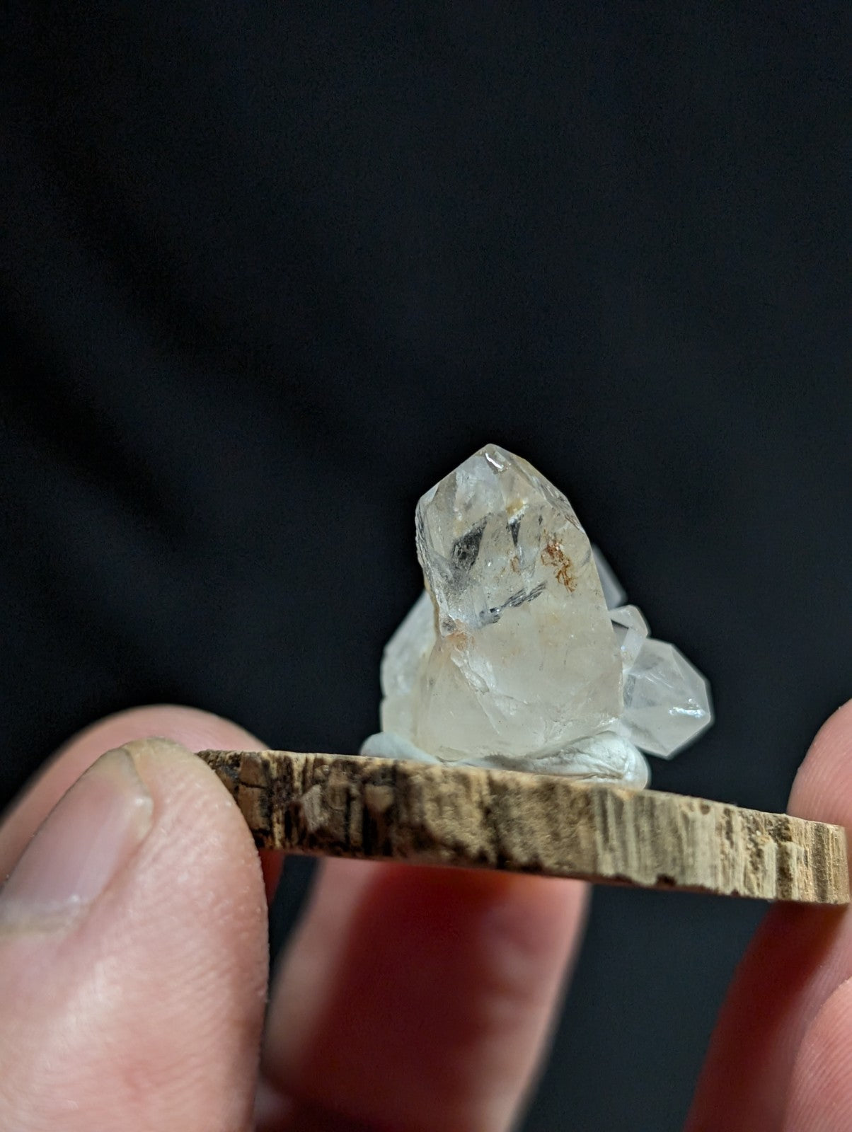 A clear, faceted quartz crystal cluster with subtle brown inclusions rests atop a rustic wooden slice.