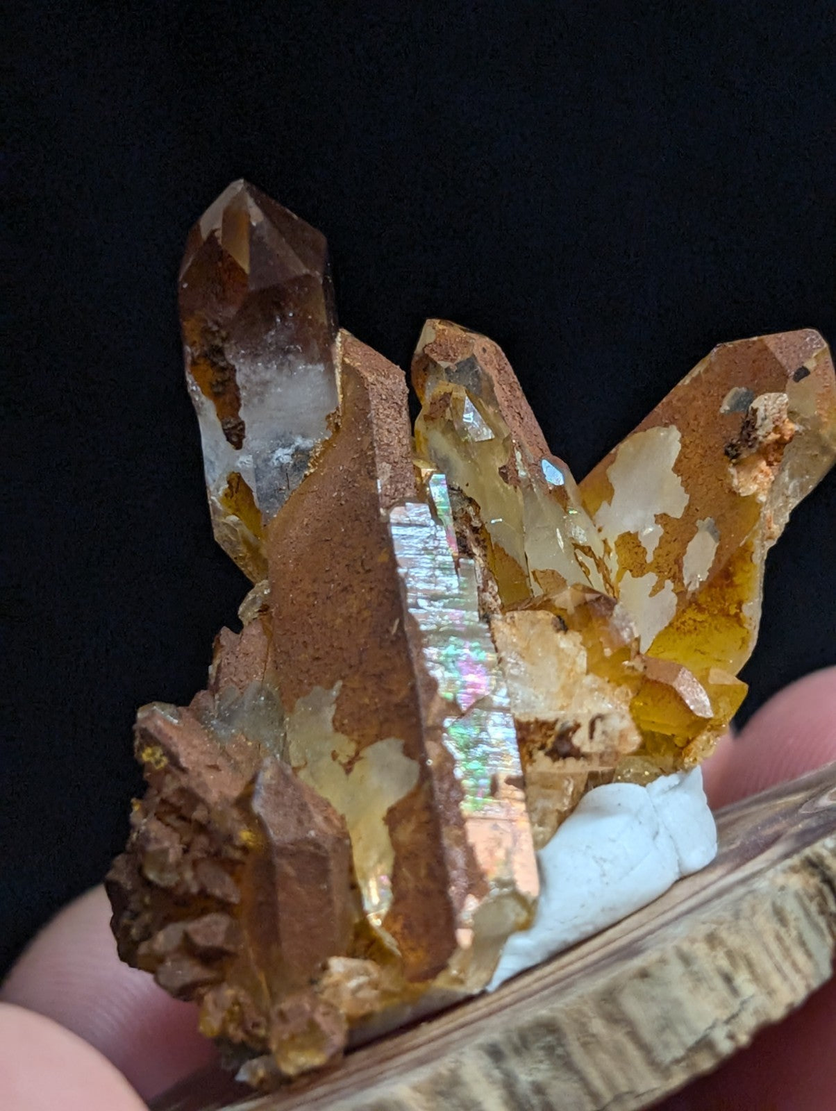 A cluster of golden-brown quartz crystals with iridescent metallic inclusions, displayed on a rustic wooden base.