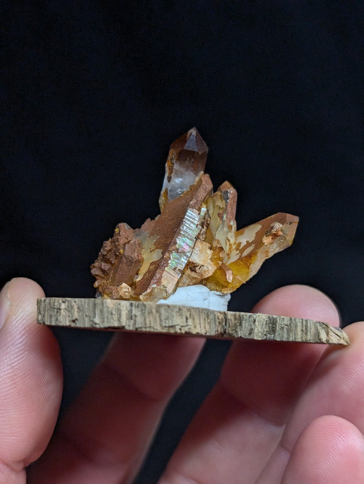 A cluster of translucent amber and golden citrine crystals with iridescent striations, mounted on a rustic wooden base.