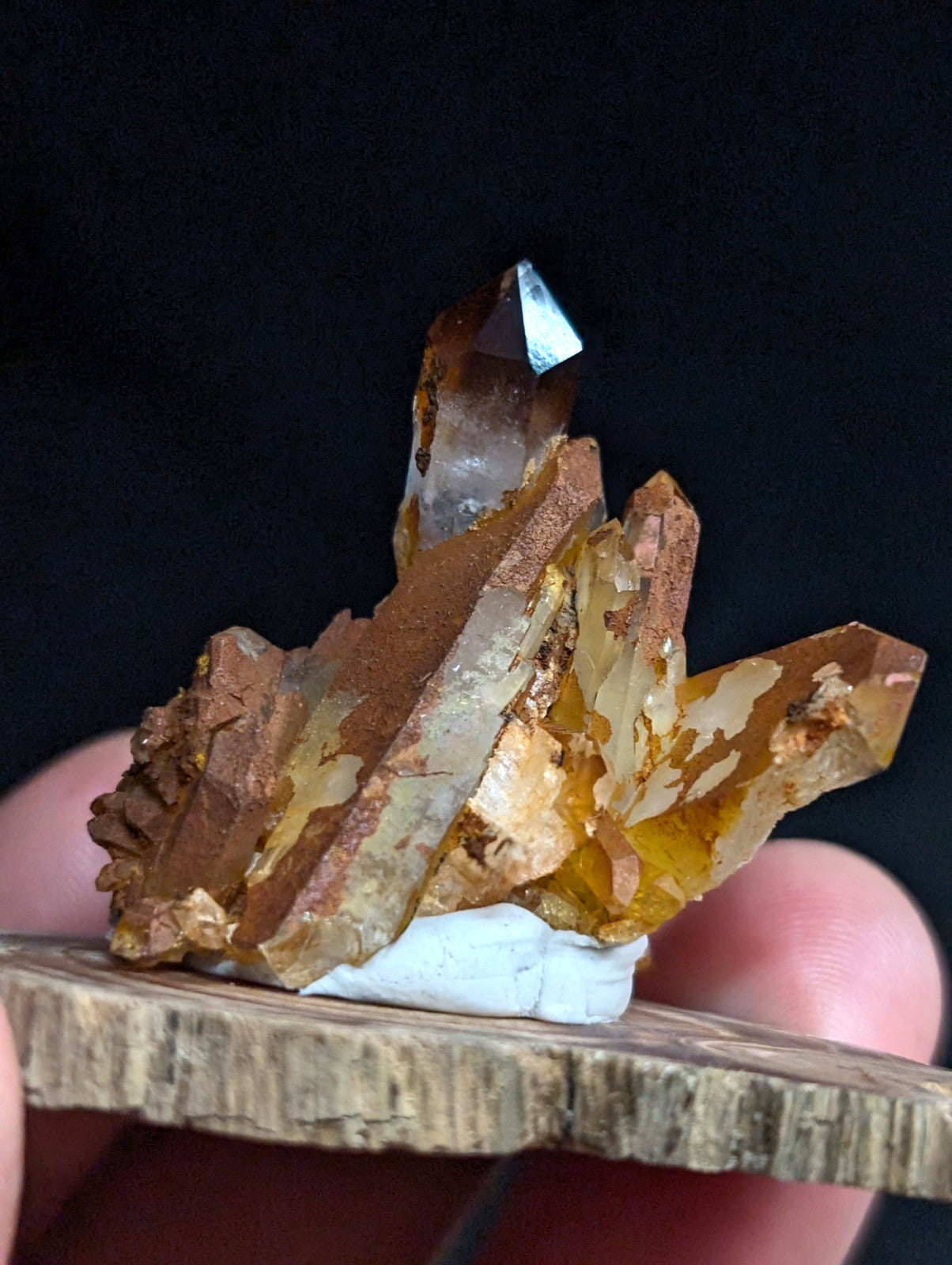 A translucent amber-colored crystal cluster with golden-brown mineral inclusions, mounted on a rustic wooden base.