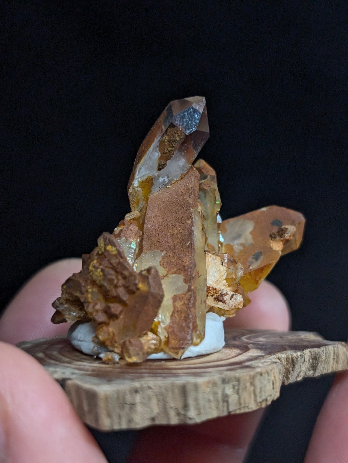 A cluster of translucent amber and golden quartz crystals with metallic inclusions, mounted on a rustic wooden slice.