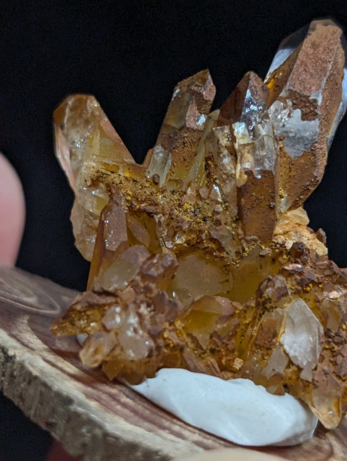 A cluster of translucent golden-yellow quartz crystals with a rough, earthy matrix and some white crystalline formations.
