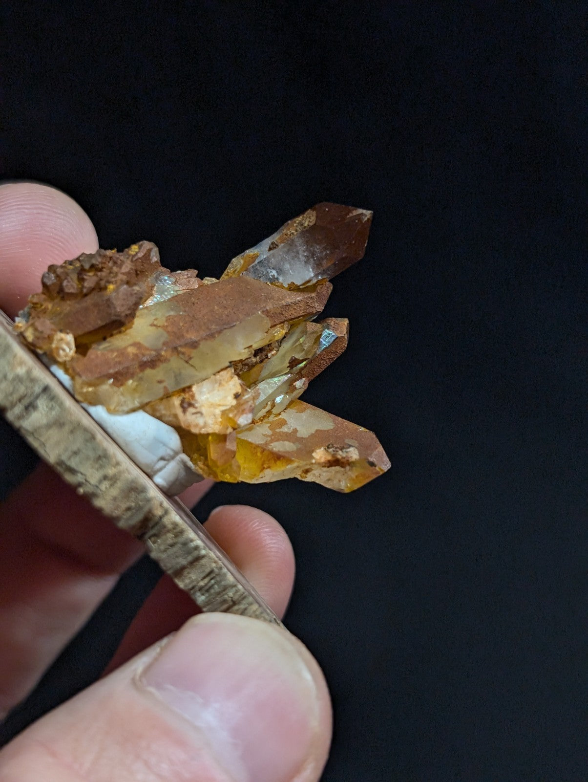 A cluster of translucent amber-colored quartz crystals with golden-brown mineral inclusions, held between fingers.
