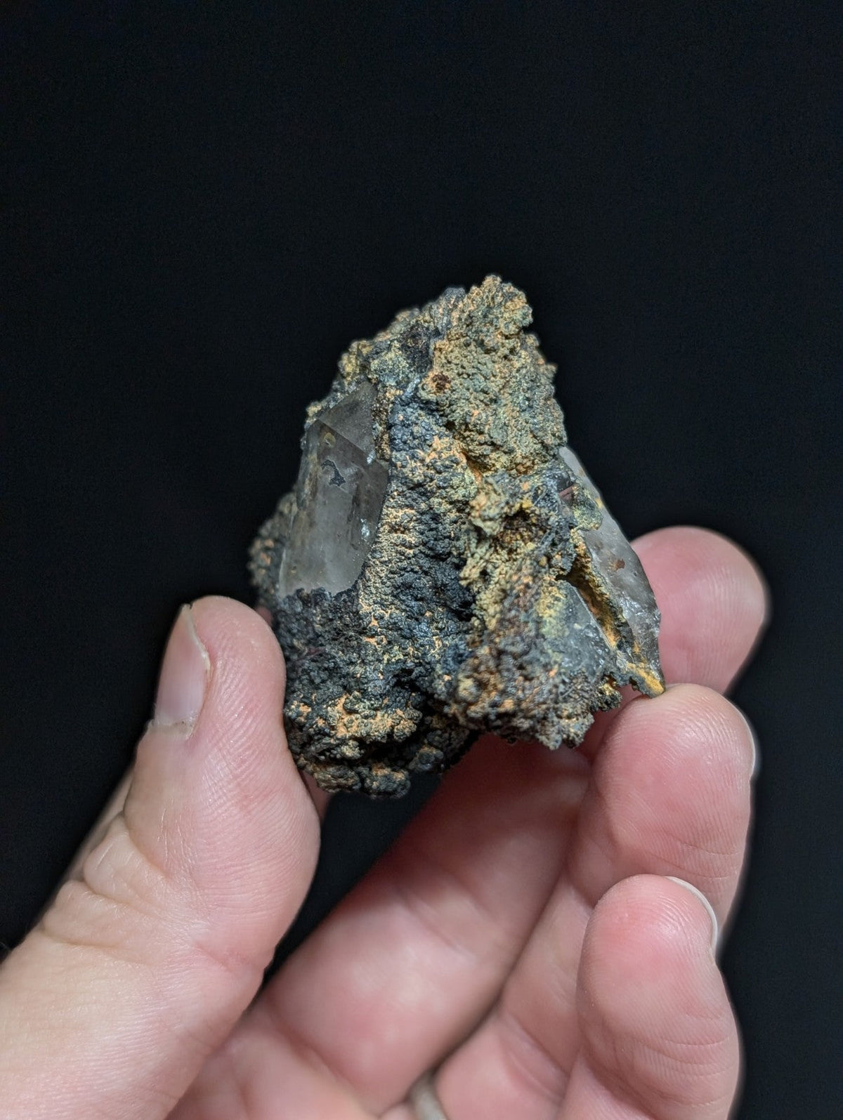 A rough, naturally formed crystal specimen with translucent clear quartz embedded in a dark gray and yellowish mineral matrix.
