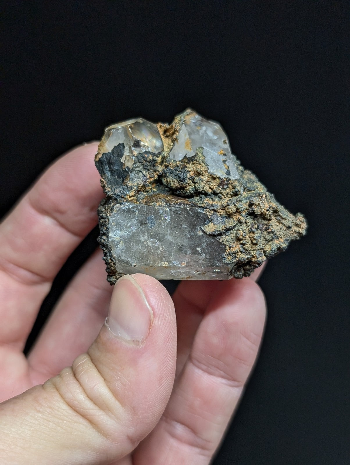 A translucent quartz crystal cluster with a rough, earthy matrix of dark and brownish material.