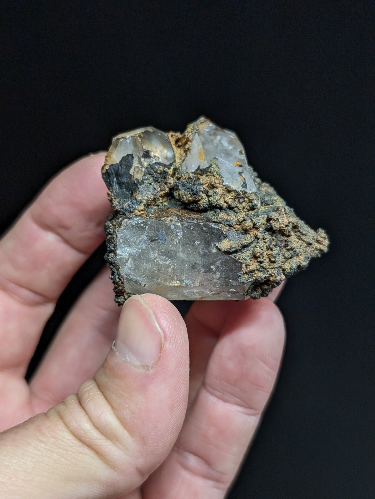 A translucent quartz crystal cluster with a rough, earthy matrix of dark and brownish material.
