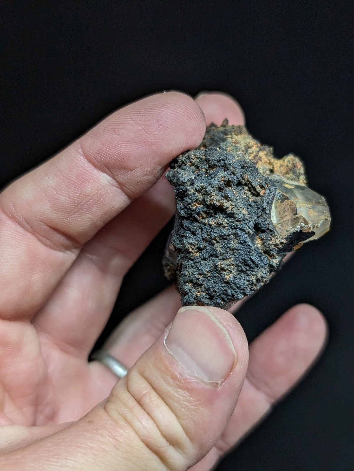 A rough, dark gray rock with a translucent crystal protruding from its surface.