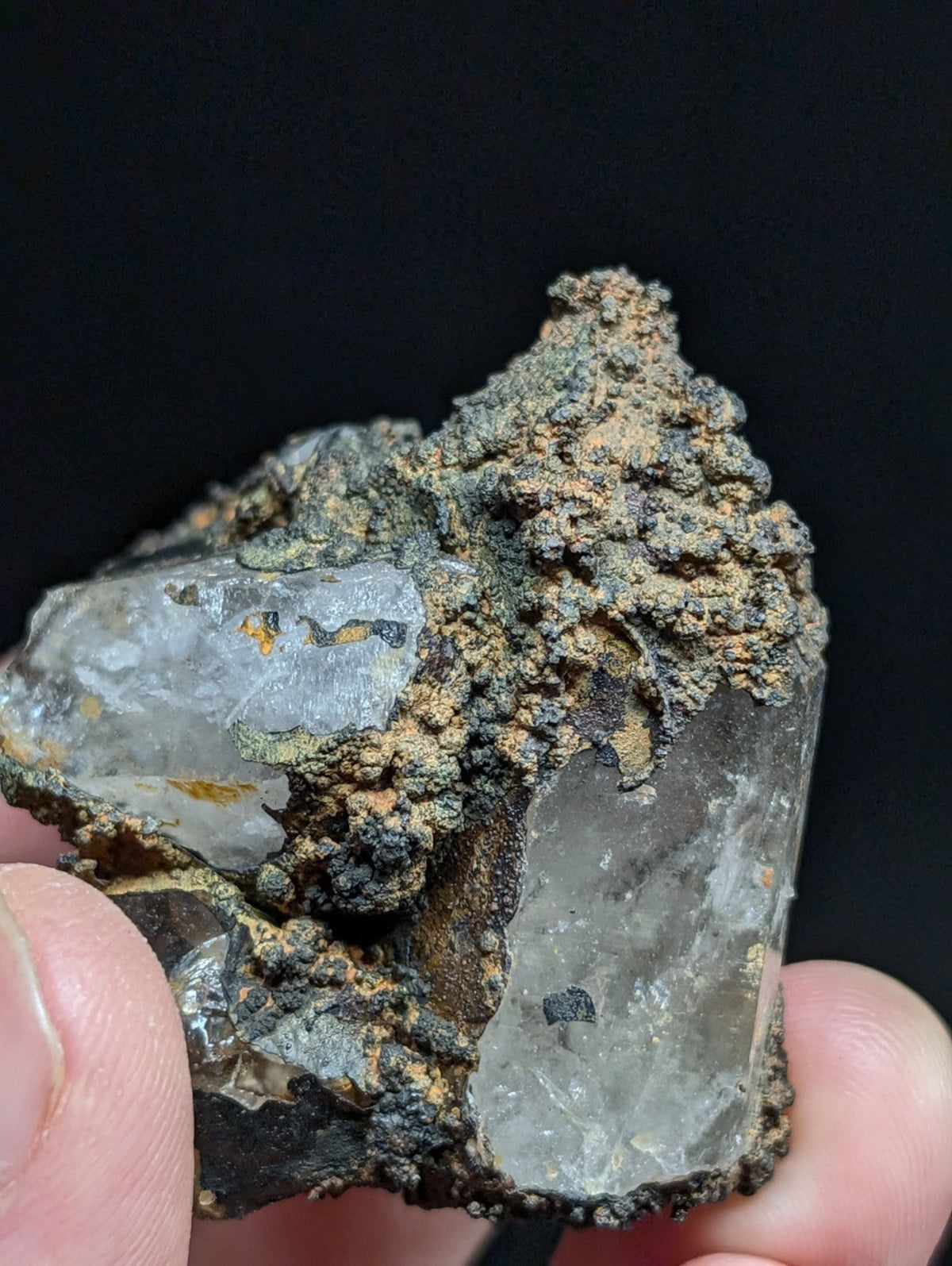A translucent quartz crystal with a rough, earthy matrix of brown and black mineral deposits.