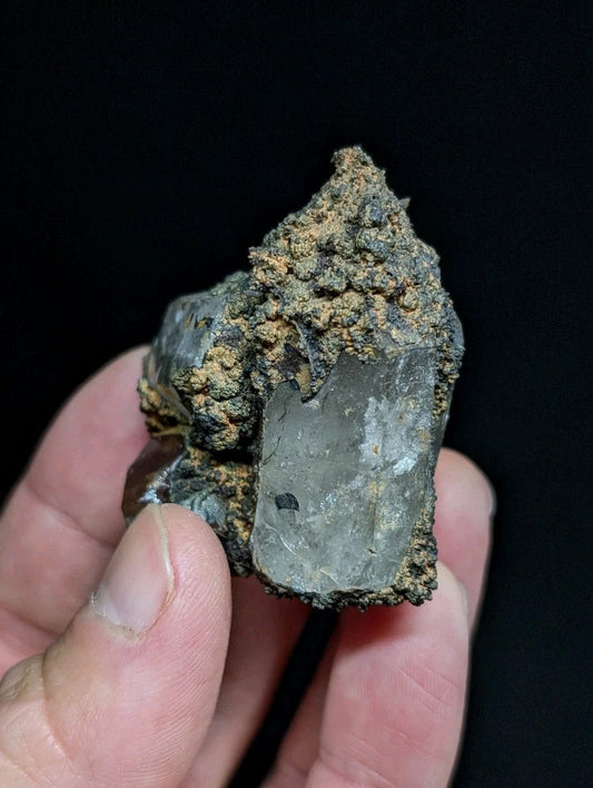 A translucent, grayish quartz crystal with rough, earthy matrix surrounding it.