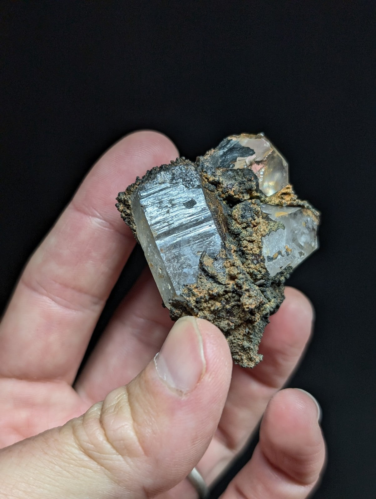 A translucent, clear quartz crystal with striations and a rough, earthy matrix holding it together.