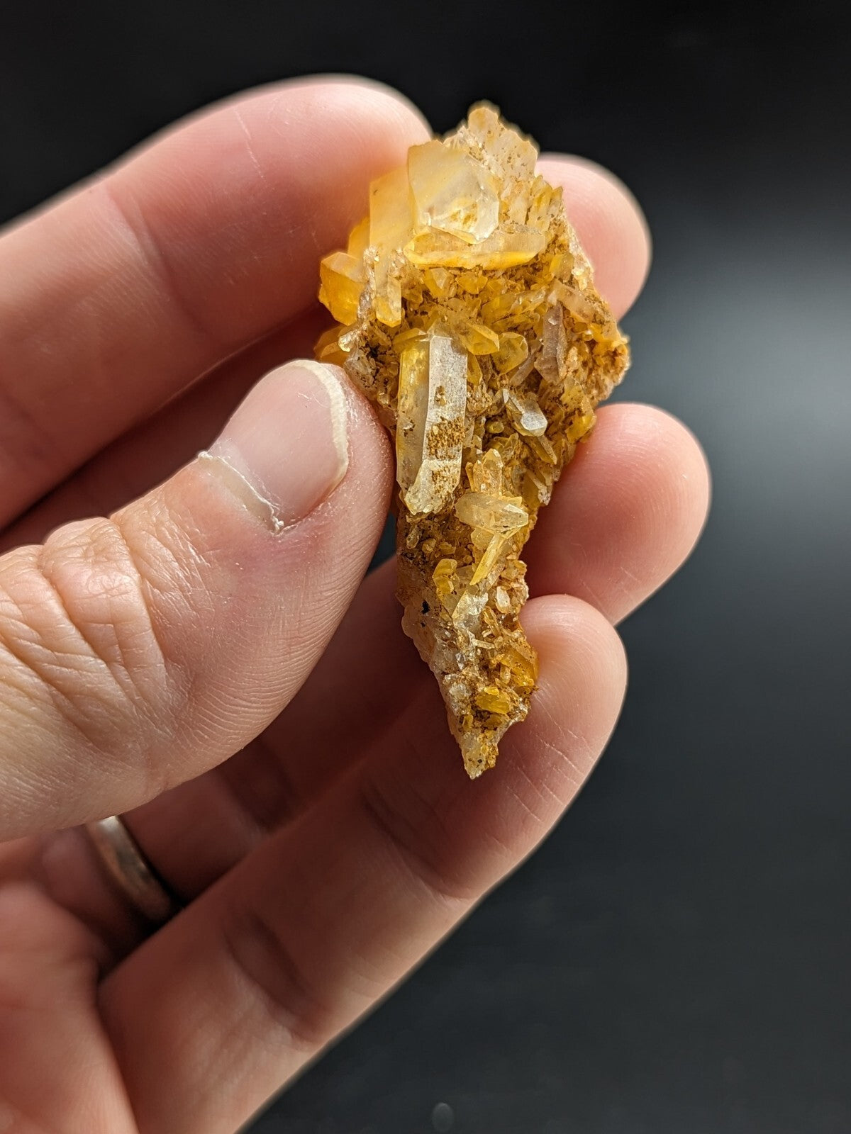 A hand holds a cluster of translucent golden-yellow crystals with sharp, faceted edges and embedded clear quartz points.
