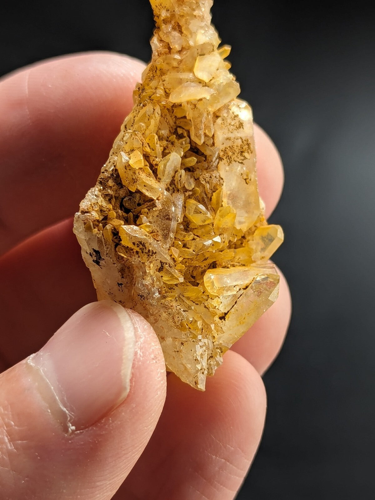 A hand holds a cluster of translucent yellow crystals with sharp, faceted edges and subtle golden inclusions.