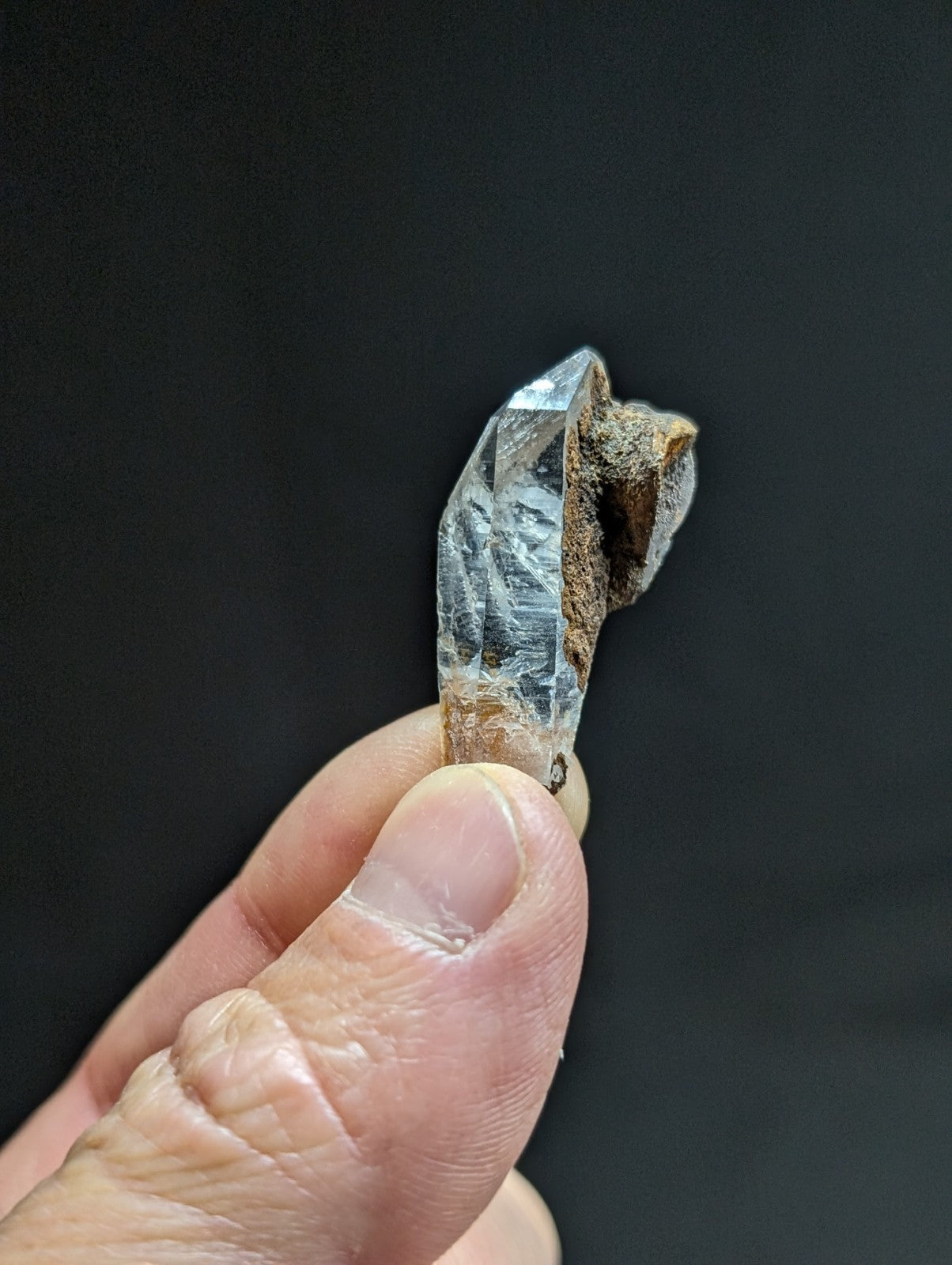 A clear quartz crystal with a rough, earthy brown base and sharp, faceted points.