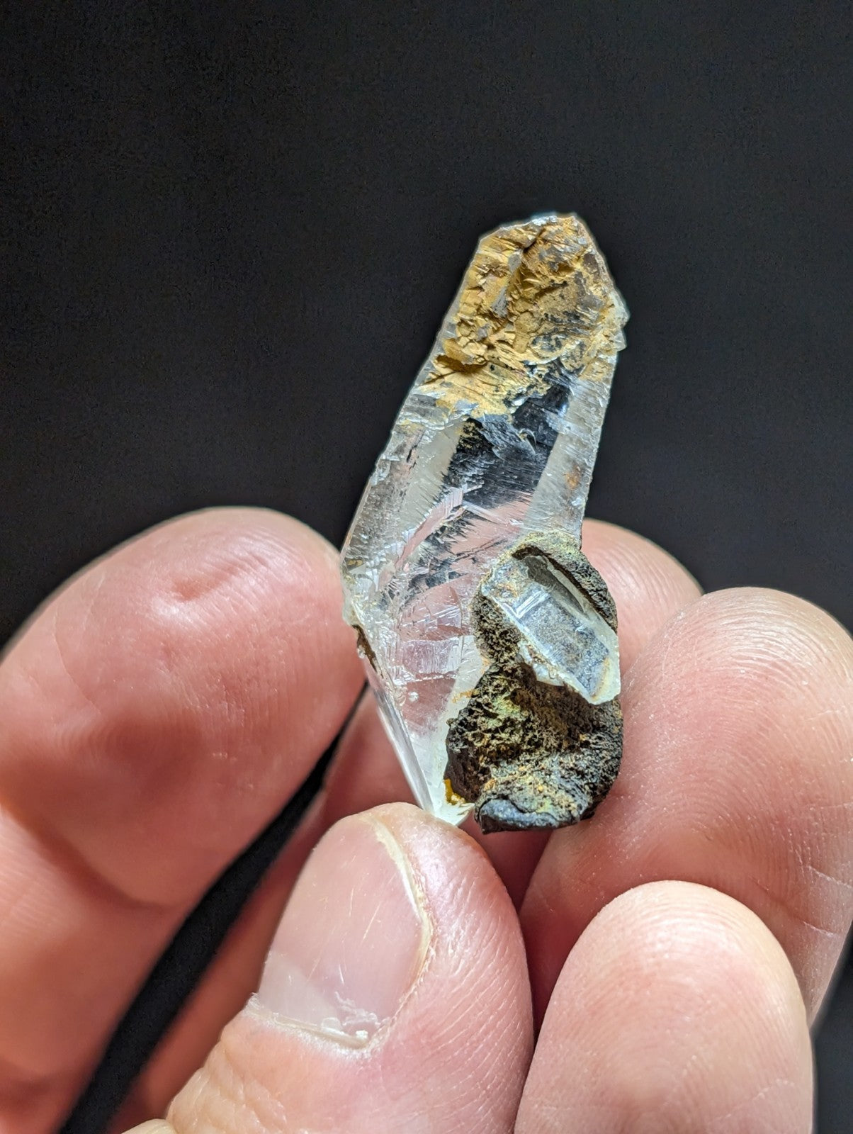 A clear quartz crystal with a rough, earthy matrix of brown and black mineral inclusions.