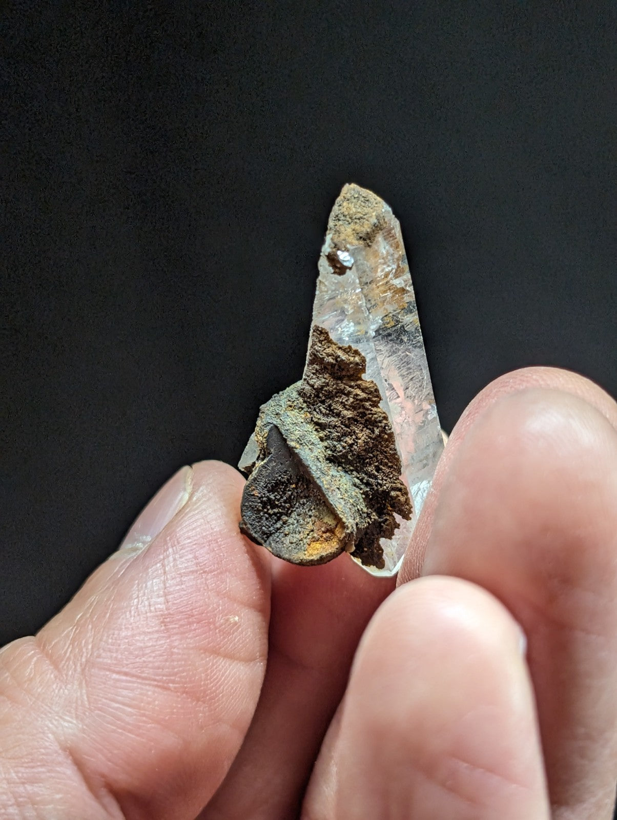 A translucent quartz crystal with a pointed tip, featuring natural brown and black mineral inclusions along its base.