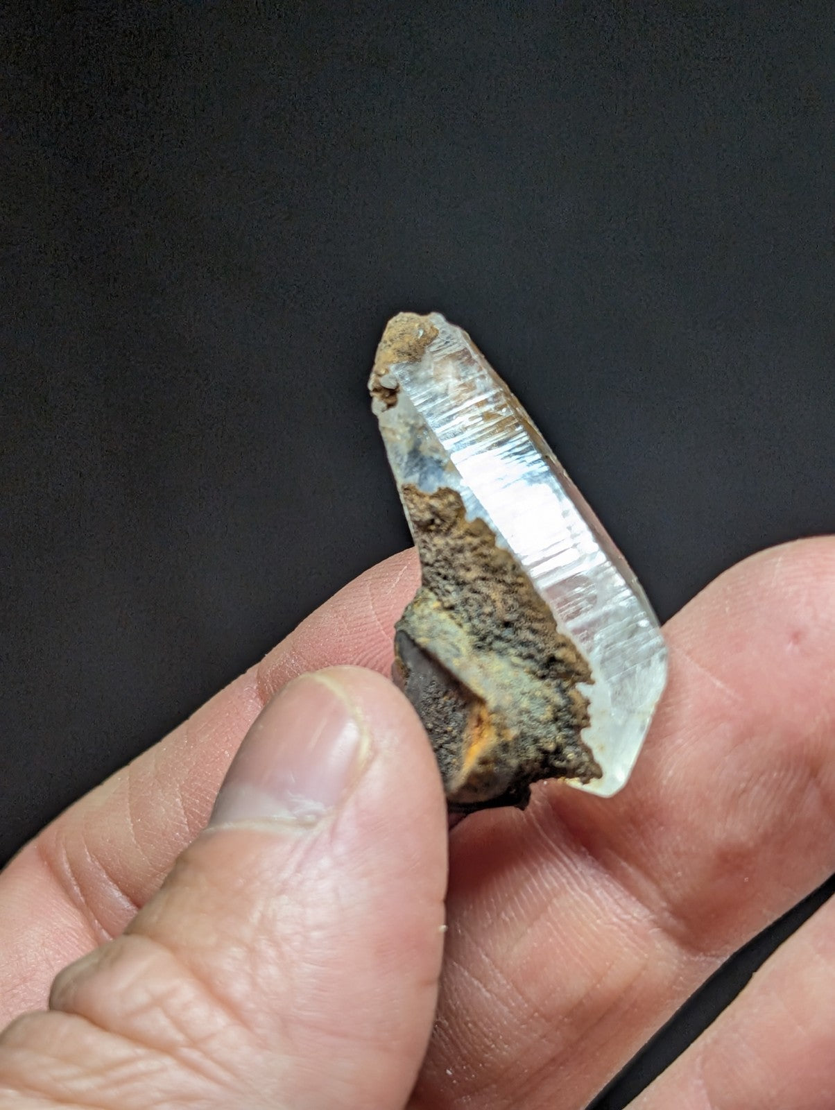 A translucent, clear quartz crystal with a rough, earthy base and visible striations along its surface.