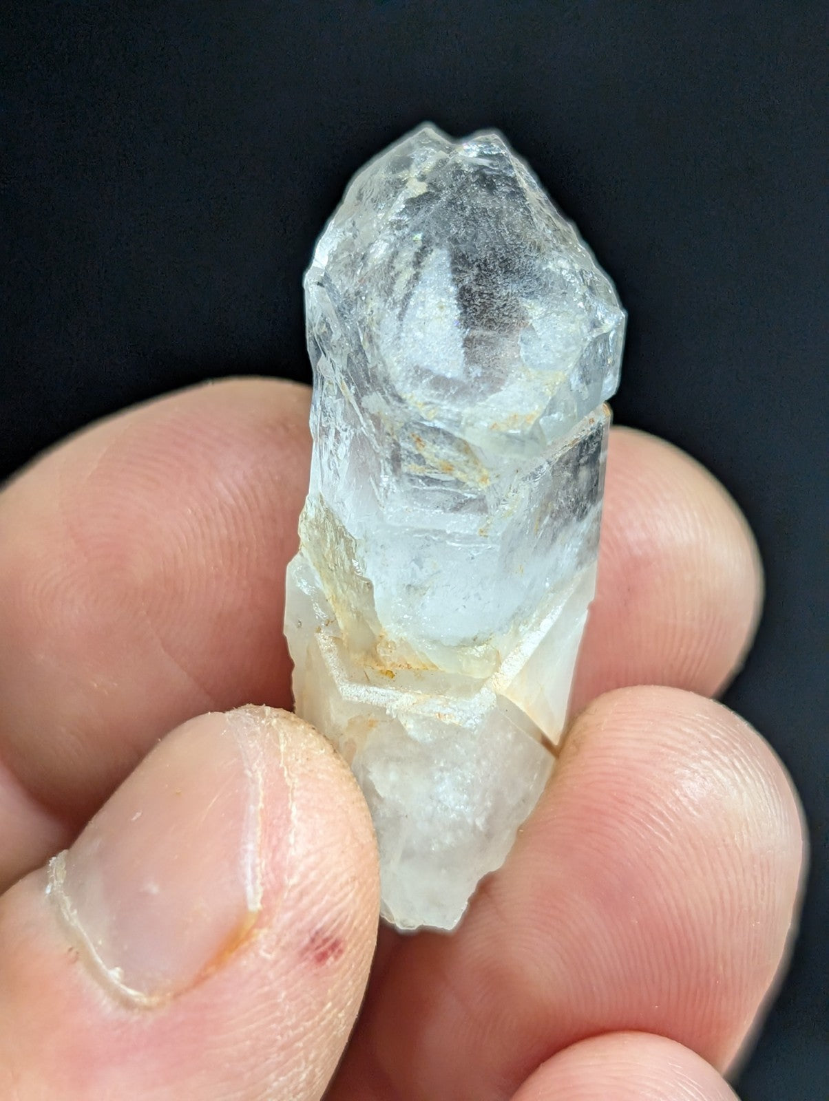 A translucent, clear quartz crystal with a rough, faceted surface and subtle yellowish inclusions near its base.