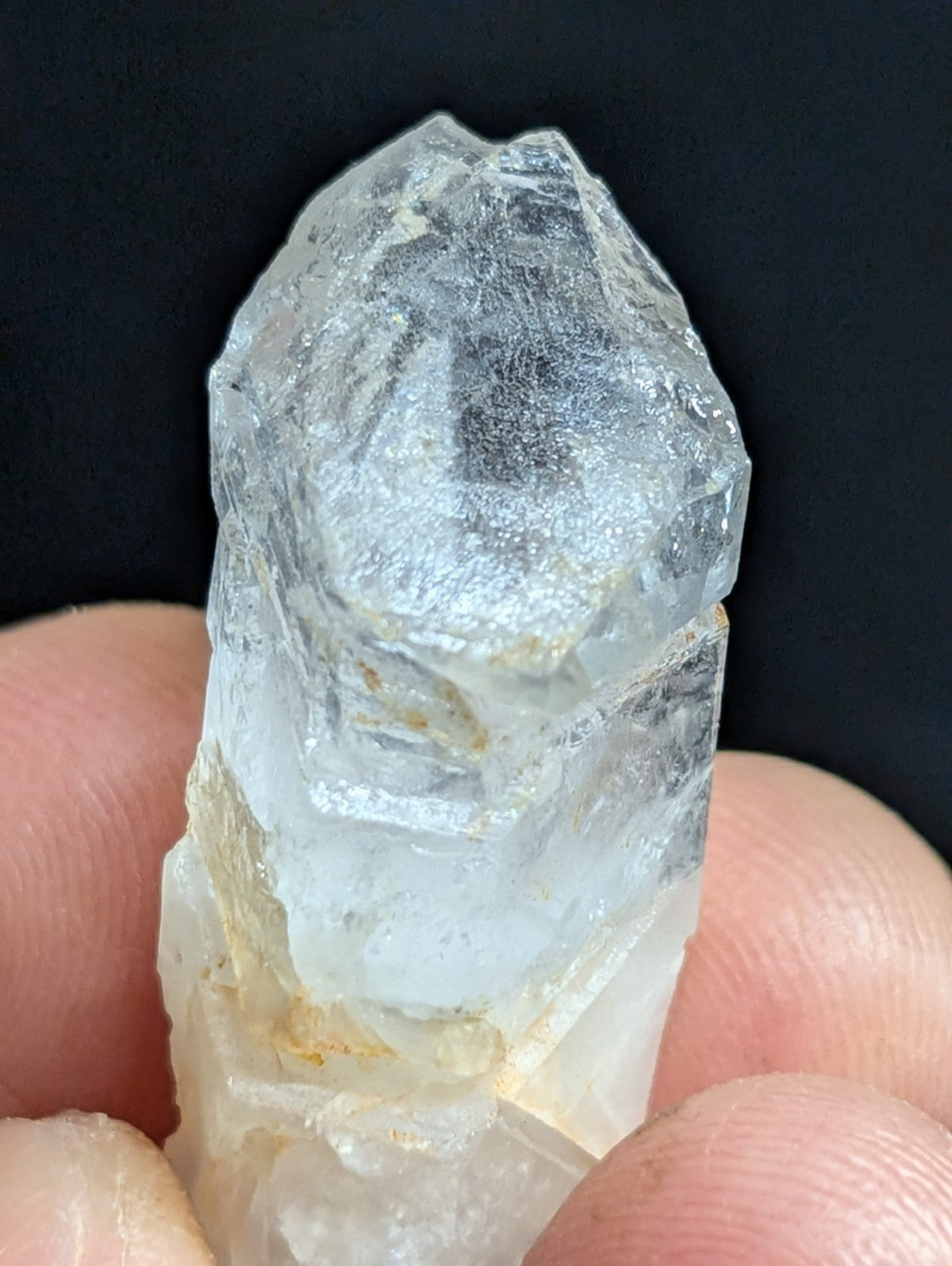 A translucent, clear quartz crystal with a rough, faceted top and a slightly cloudy base held between fingers.