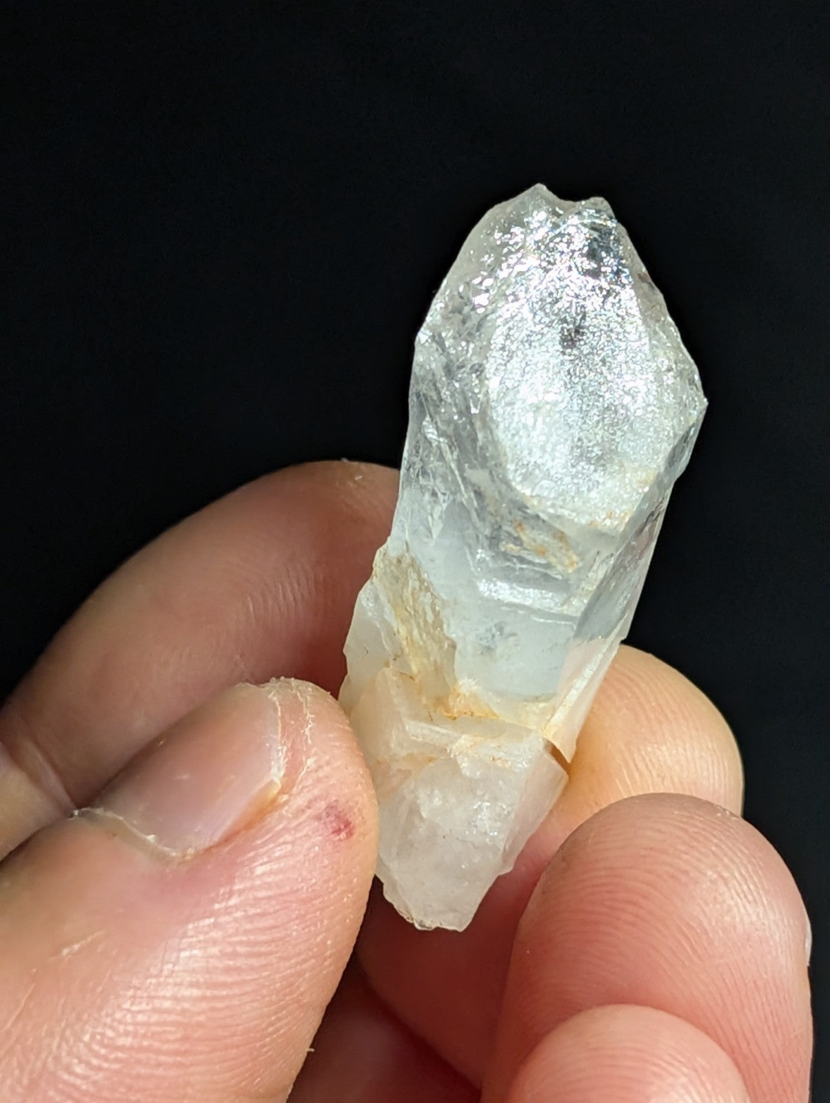 A translucent, pale quartz crystal with a faceted top and rougher base held gently in fingers.