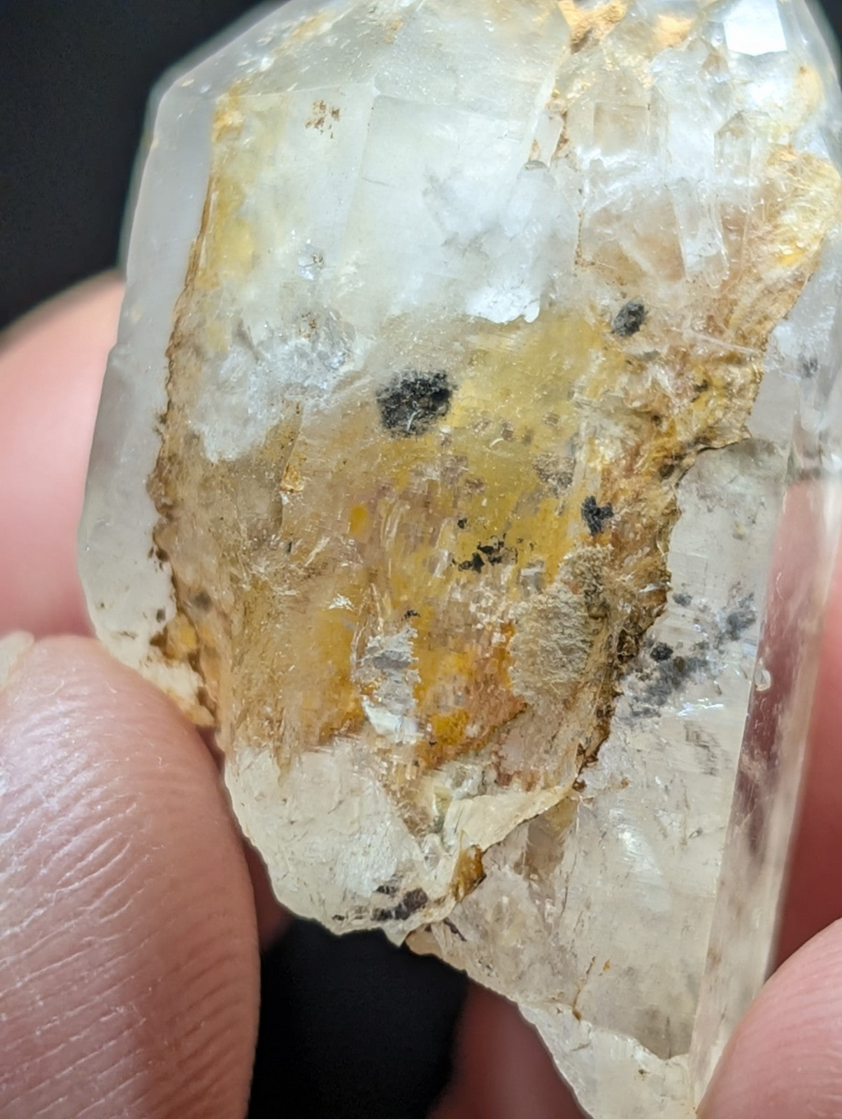 A translucent quartz crystal with a rough, natural surface featuring patches of yellow and black inclusions.