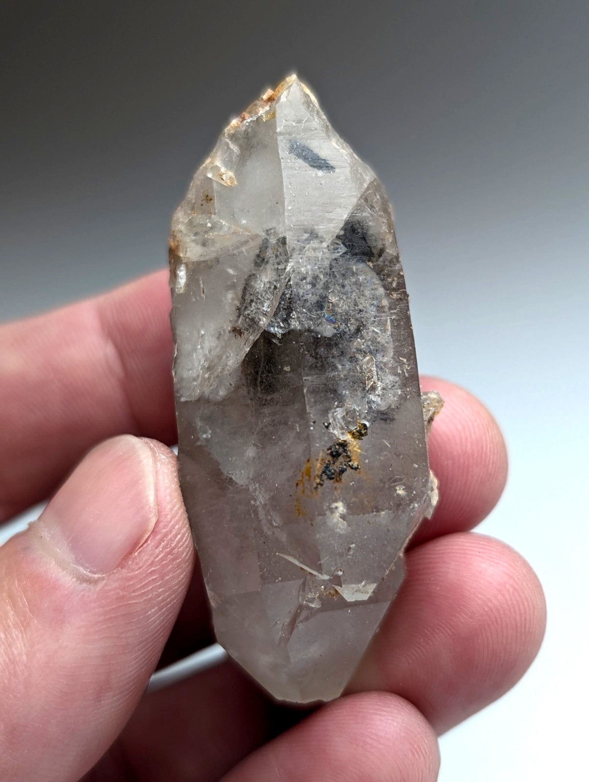 A unique translucent quartz crystal with nacrite inclusions and a pointed tip held gently between fingers from Arkansas