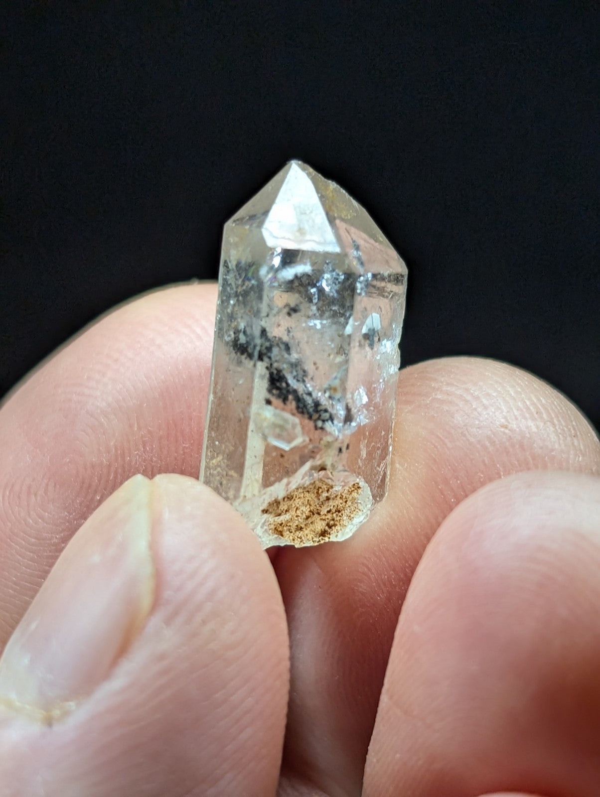 A clear quartz crystal with a pointed tip and natural inclusions, held gently between fingers.